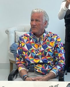 A person sitting in a chair, wearing a long-sleeved shirt with a vibrant, geometric, multi-colored pattern.