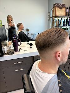 A barber cutting a client's hair in a salon, viewed from behind the client in the barber chair.