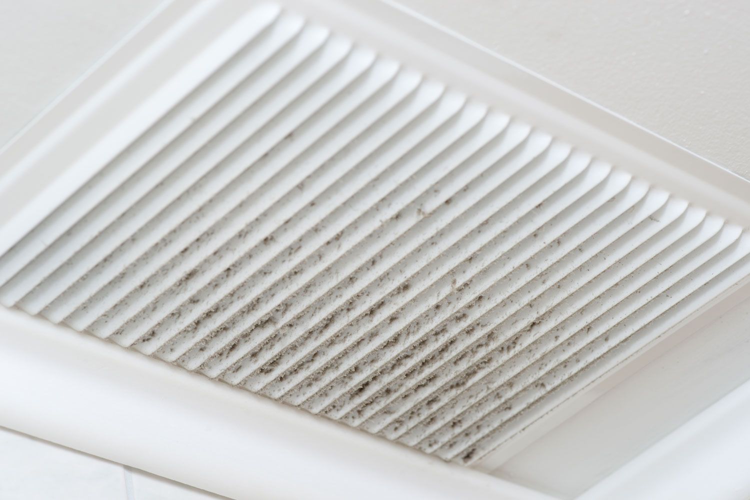 A close up of a dirty air vent in a bathroom.