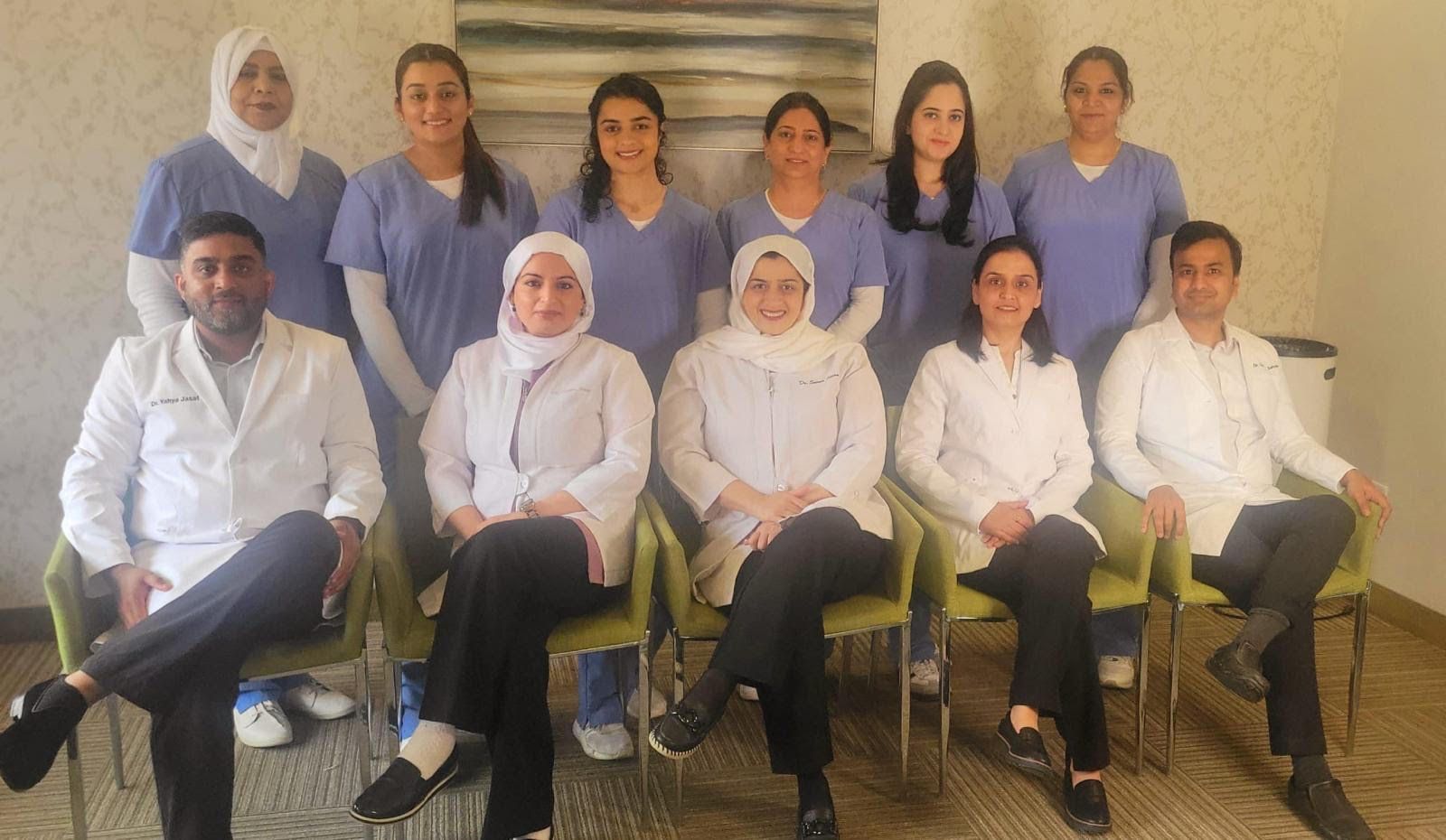 Group of doctors and nurses, wearing white coats and scrubs, smiling for a group photo in a healthcare setting.