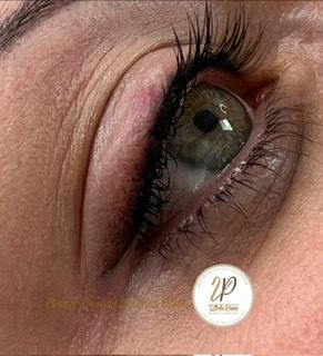 Nahaufnahme eines grünen Auges mit langen Wimpern und rosa Lidschatten auf geschlossenem Lid