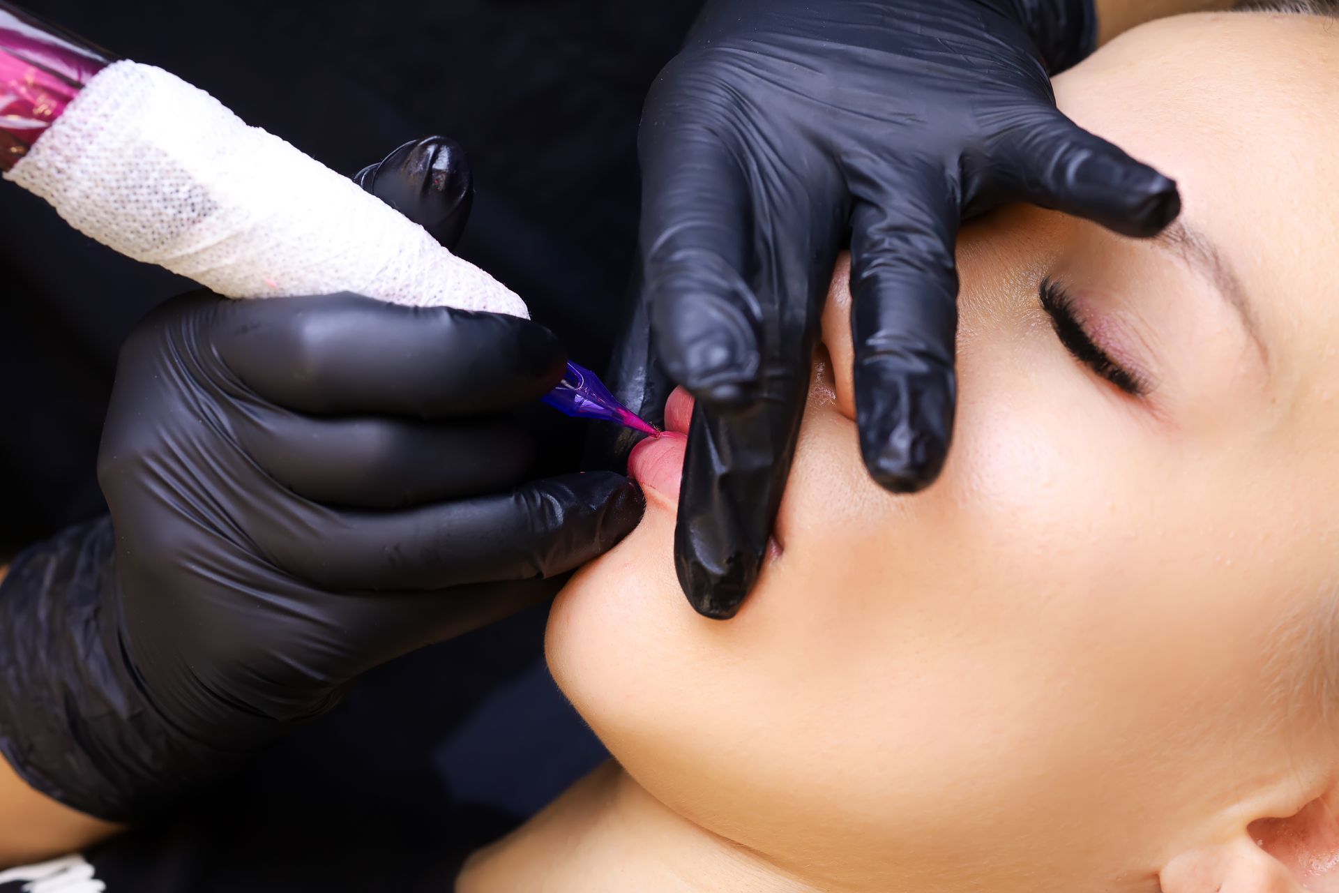 Behandschuhte Hände tragen mit einem violetten Tattoo-Stift Permanent-Make-up auf ein geschlossenes Auge auf.
