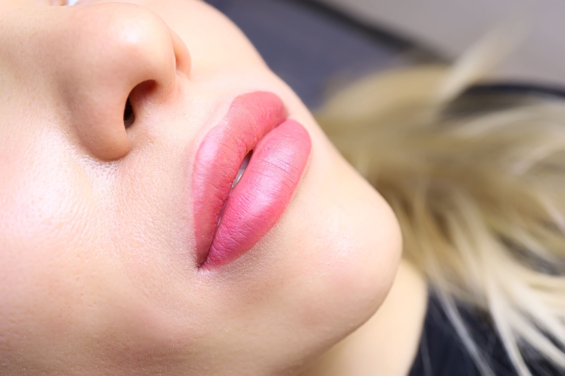 Nahaufnahme eines Gesichts mit glänzenden rosa Lippen und blonden Haaren vor einem weichen Hintergrund