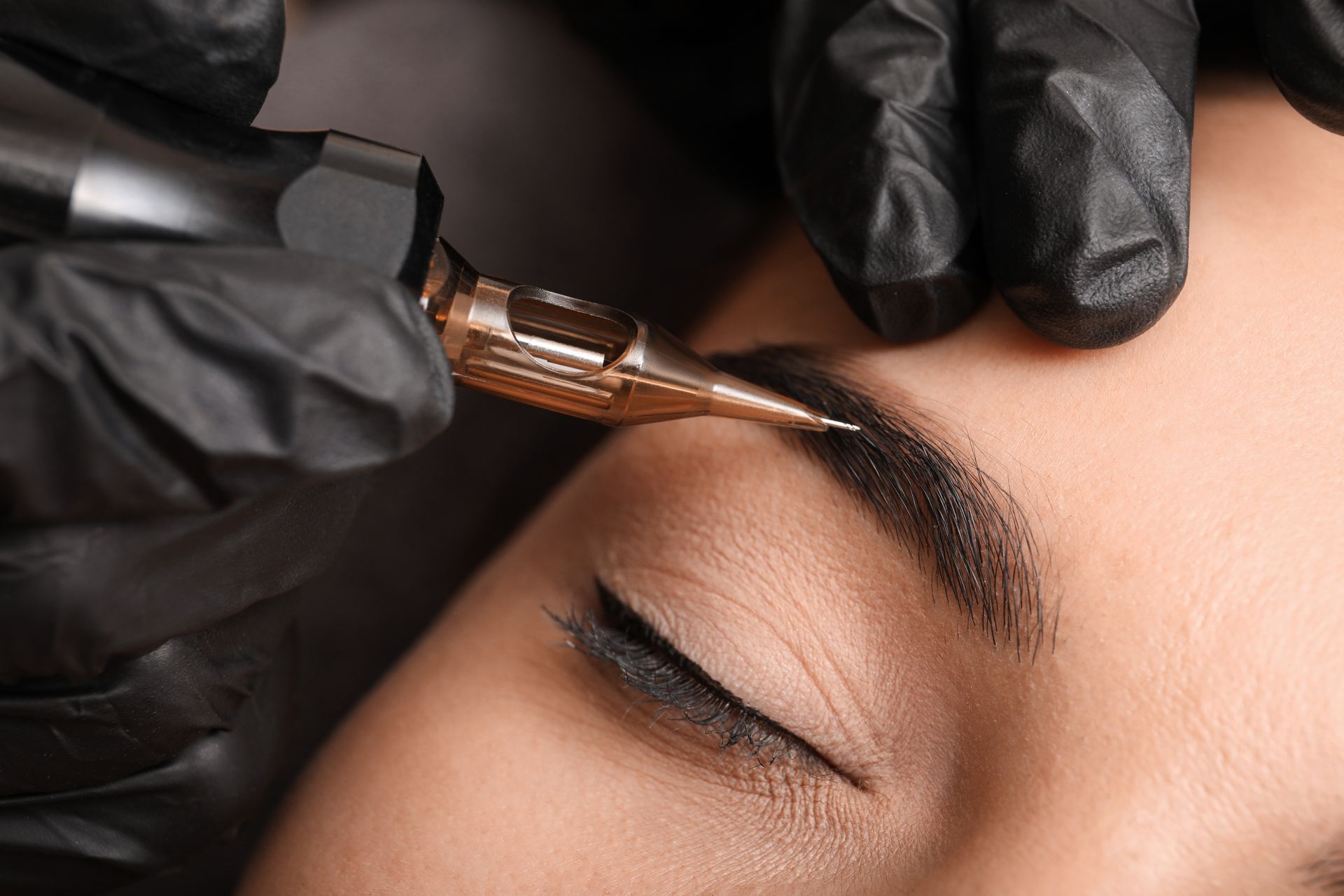 Behandschuhte Hände tragen mit einem Pinsel auf einem geschlossenen Auge Make-up auf eine Augenbraue auf.