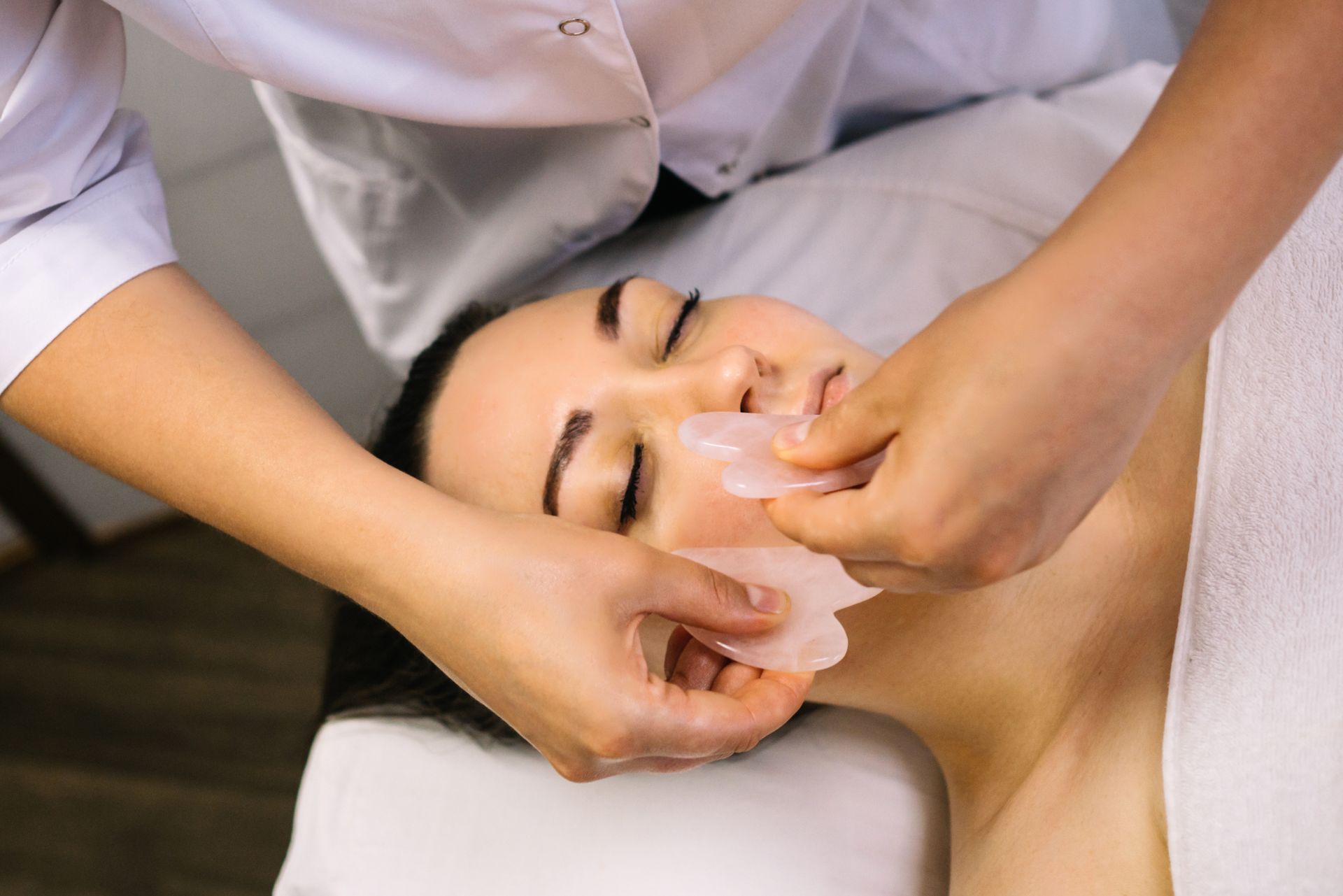 Gesichtsmassage an einer entspannten Person, die mit geschlossenen Augen liegt