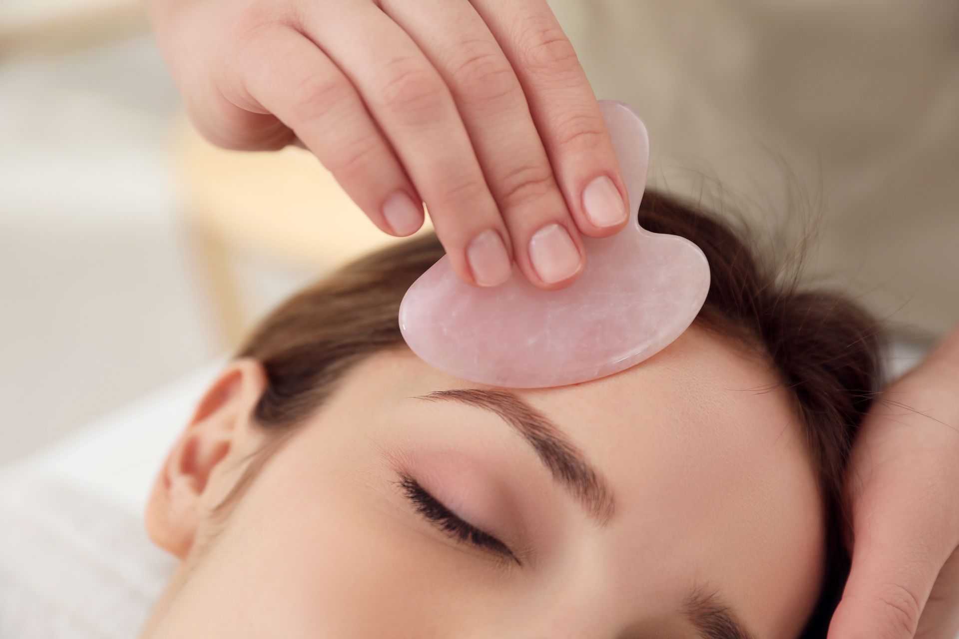 Eine Hand legt während einer Spa-Behandlung ein rosa Gesichtspad auf die Stirn einer Person.