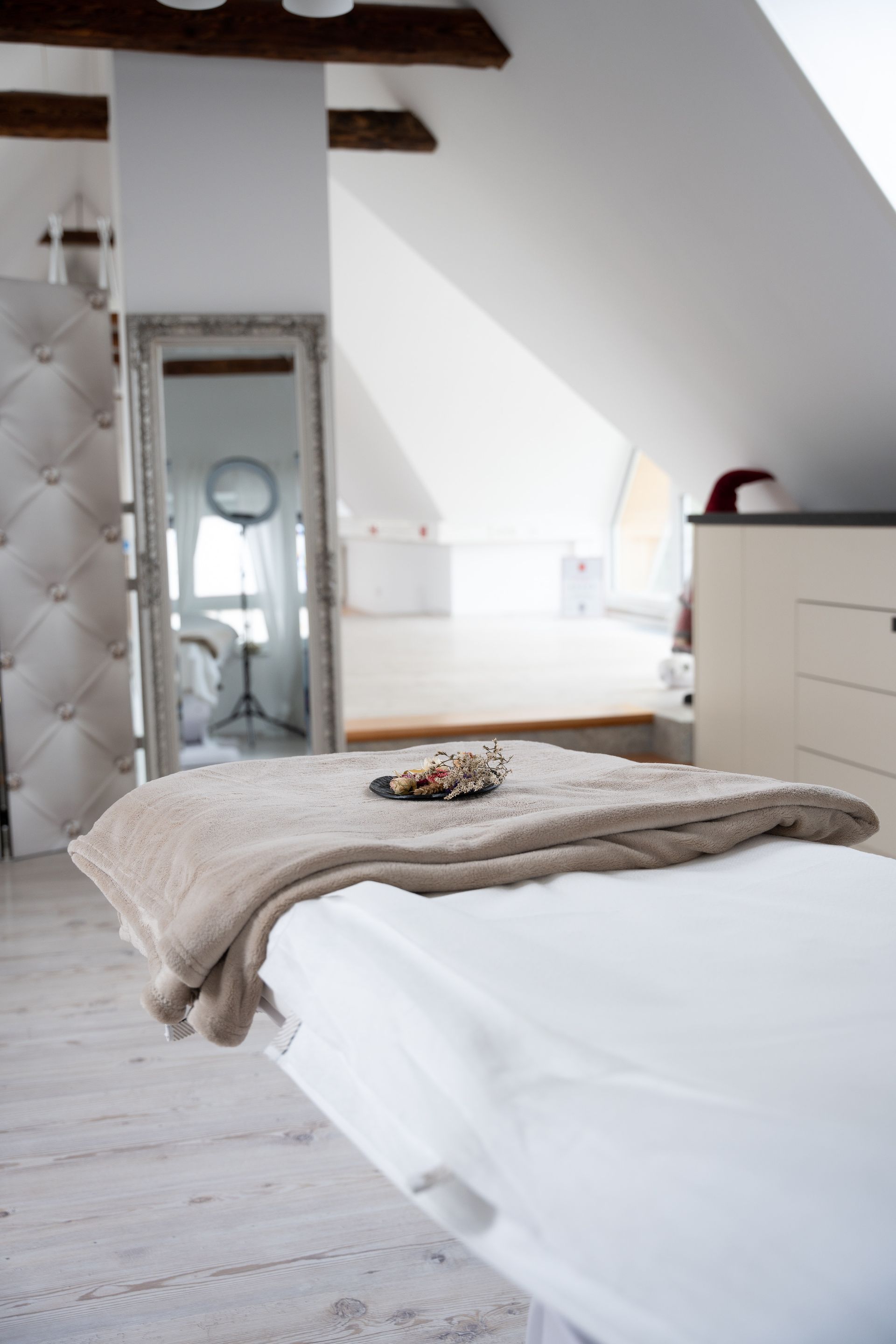 Helles Dachgeschosszimmer mit weißem Bett, Dachschräge und einer Kommode neben einem Spiegel
