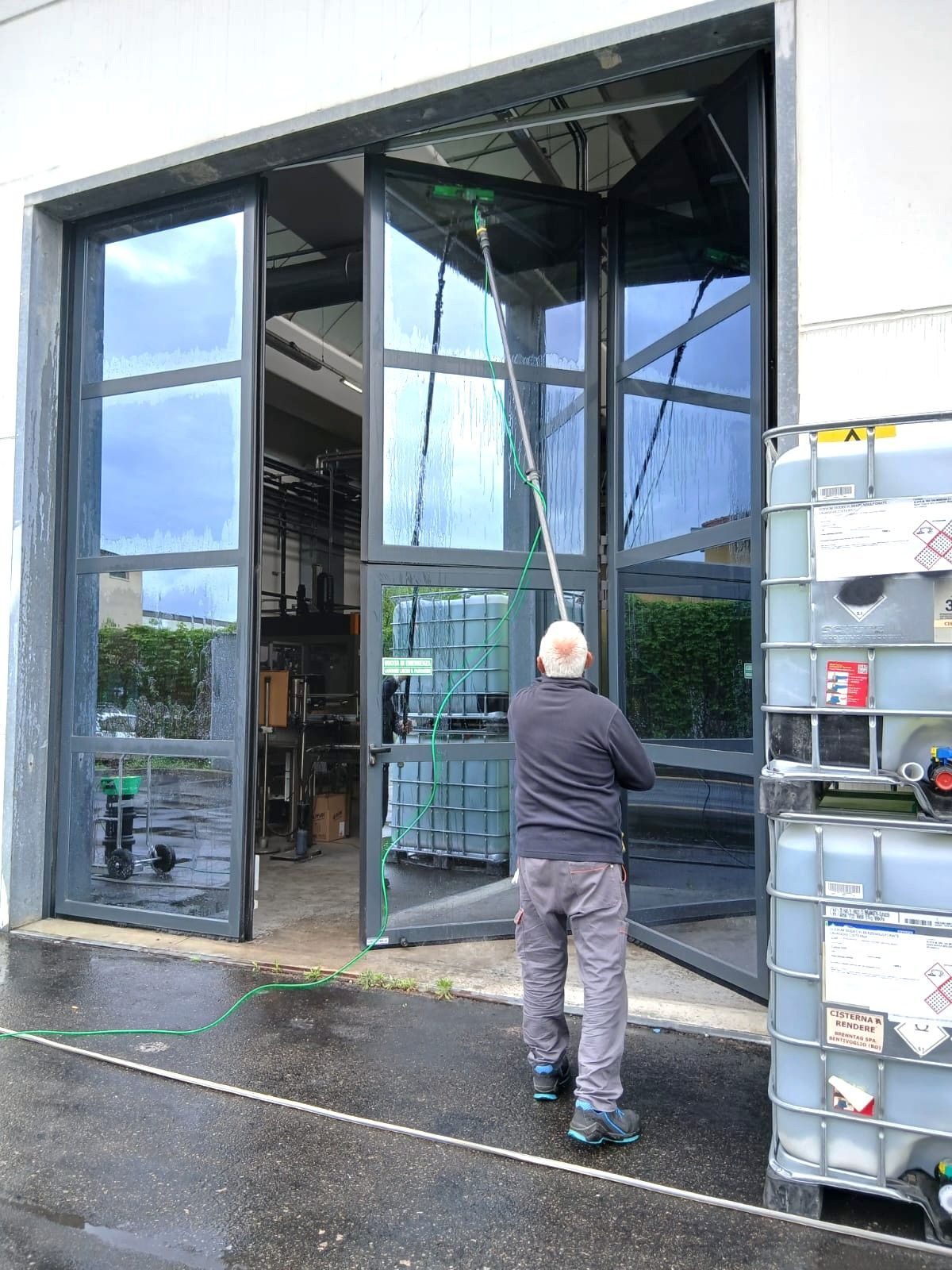 Uomo che pulisce una grande finestra con una spazzola a manico lungo fuori da un magazzino.