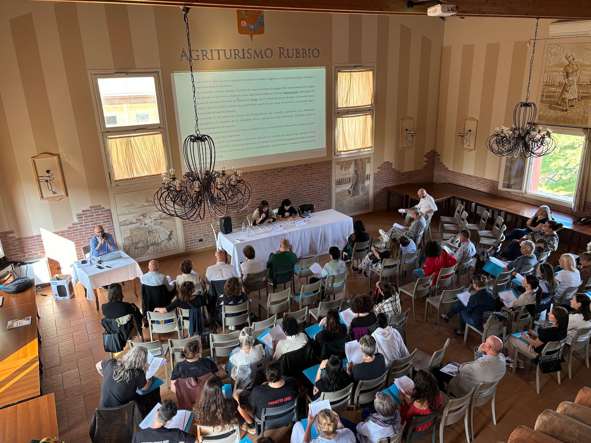 Il pubblico di una conferenza ascolta i relatori seduti a un tavolo con una presentazione di diapositive.