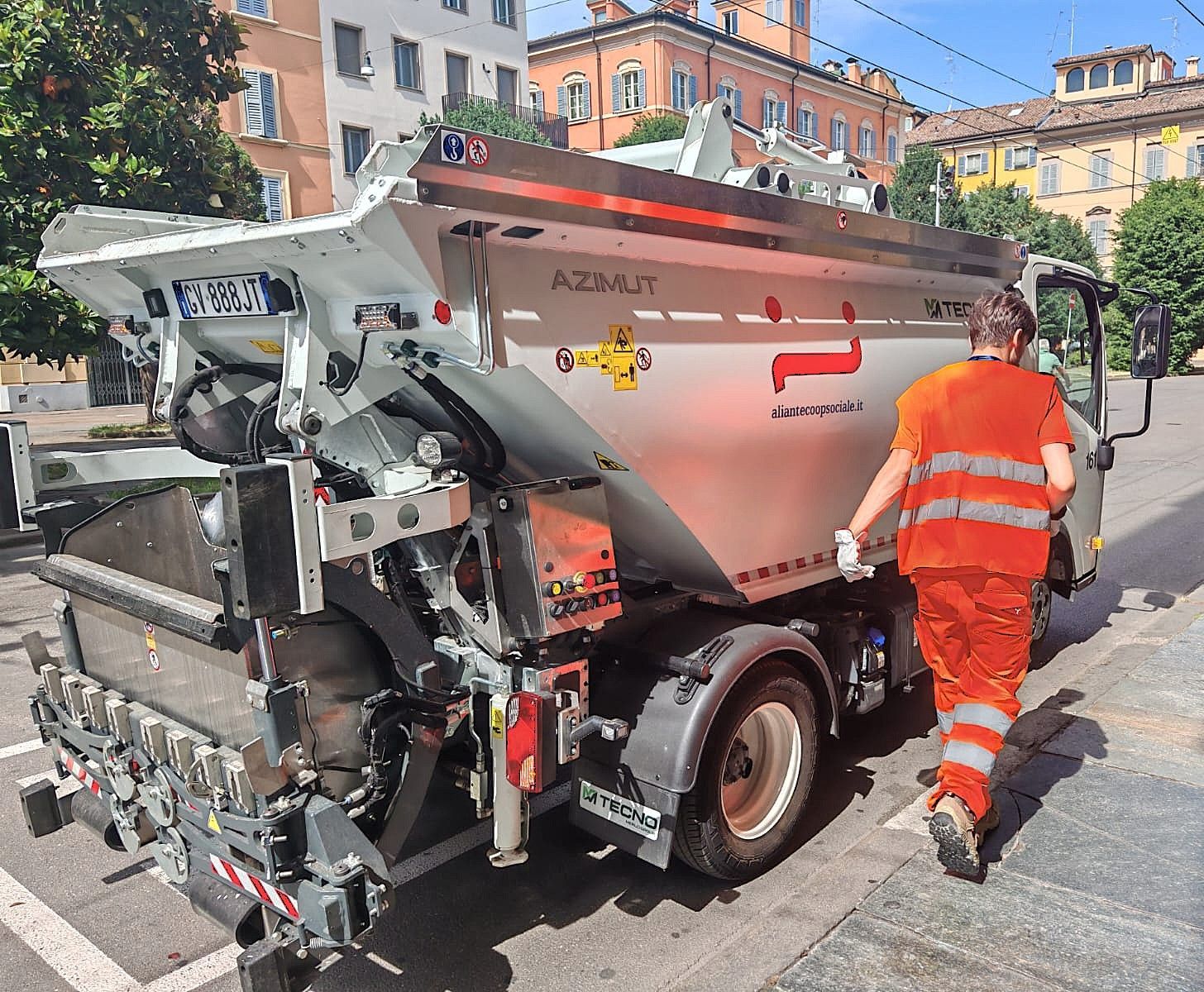 Camion per la pulizia delle strade con un operaio con il giubbotto arancione che cammina a fianco.