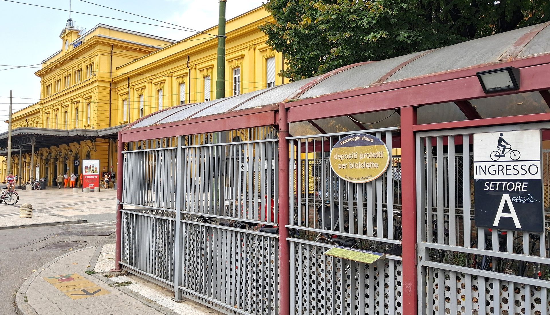 Ingresso di una stazione ferroviaria, con cancello metallico e tenda da sole. L'edificio è giallo.