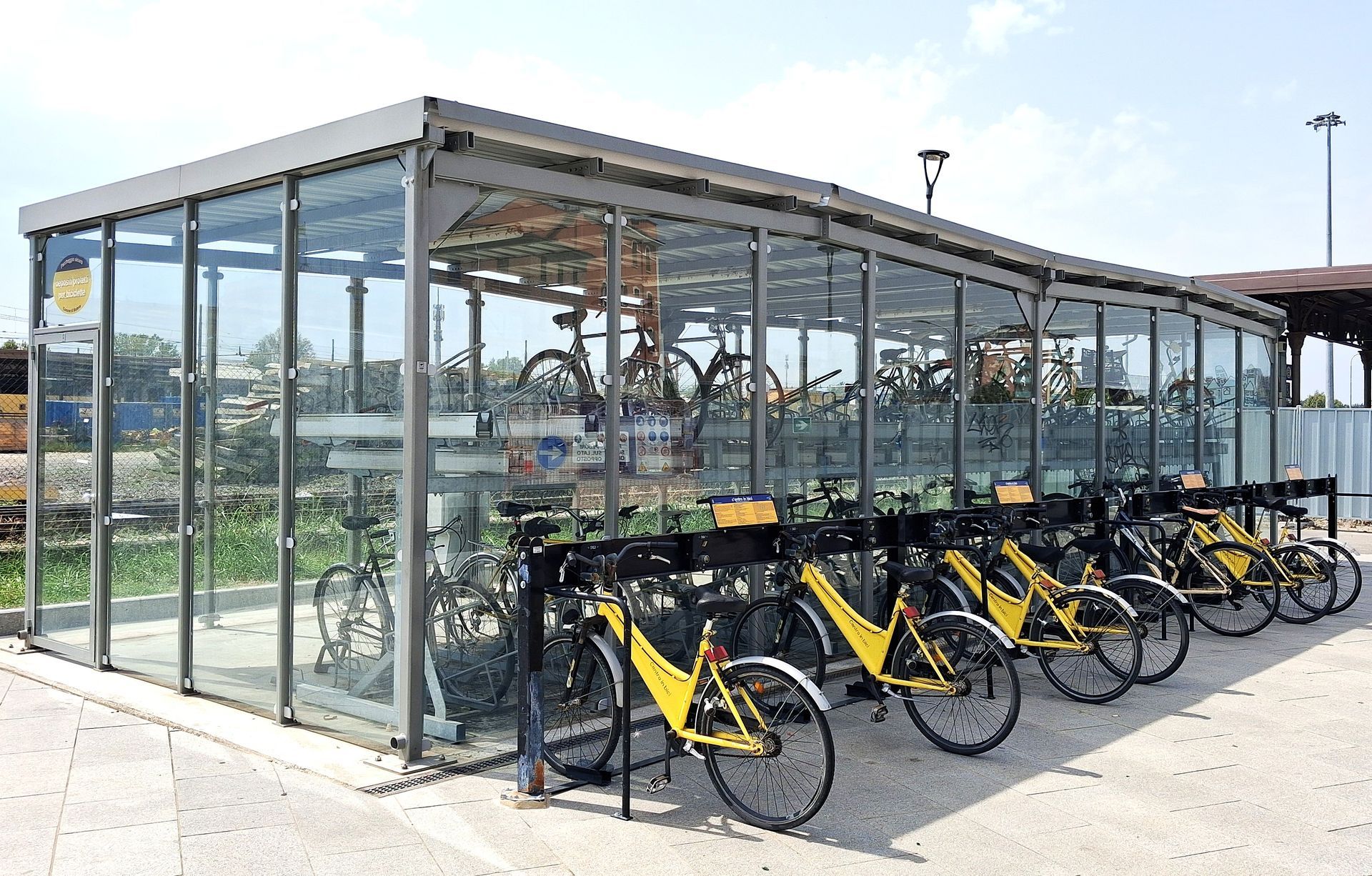 Deposito per biciclette con file di biciclette gialle parcheggiate all'esterno e all'interno, con pareti in vetro.