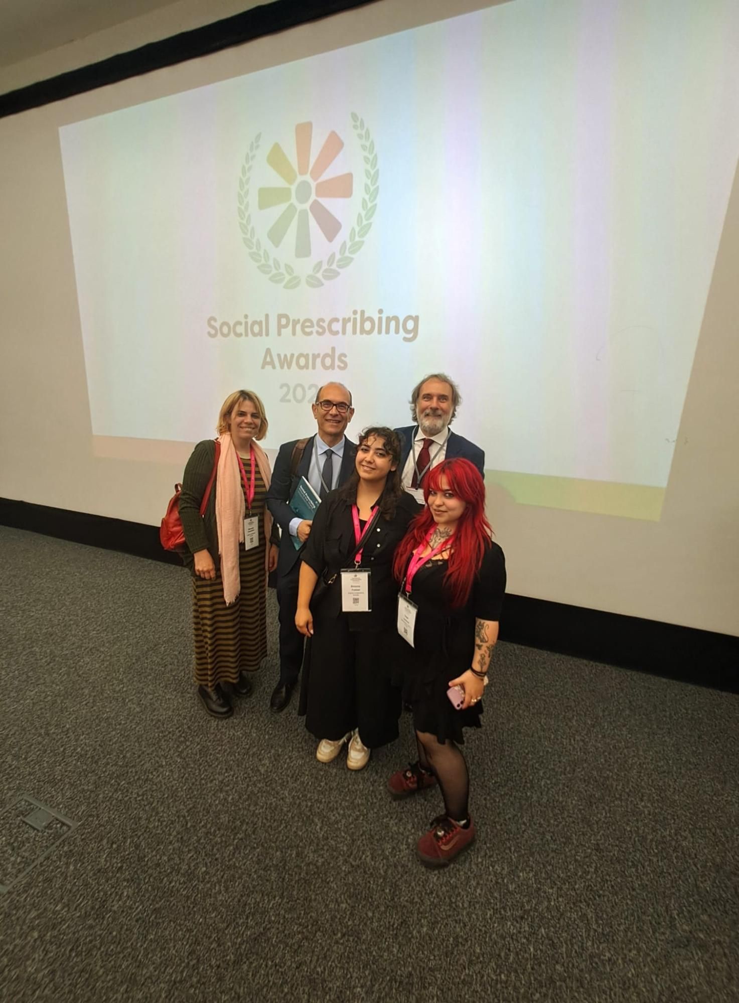 Persone in posa per una foto ai Social Prescribing Awards 2023, con un logo sullo sfondo.