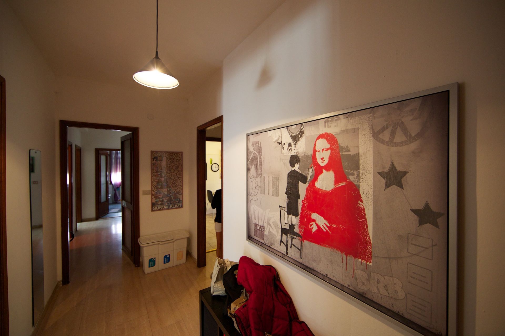 Corridoio con pavimenti in legno chiaro, porte e una grande opera d'arte raffigurante una figura rossa.