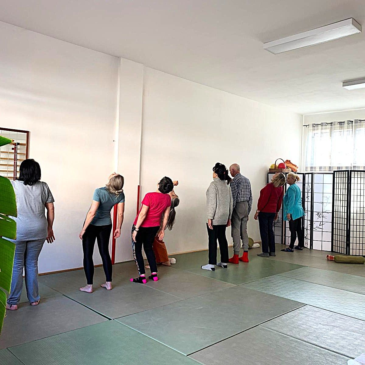 Persone che si allungano vicino a un muro in una stanza luminosa con stuoie e uno schermo.