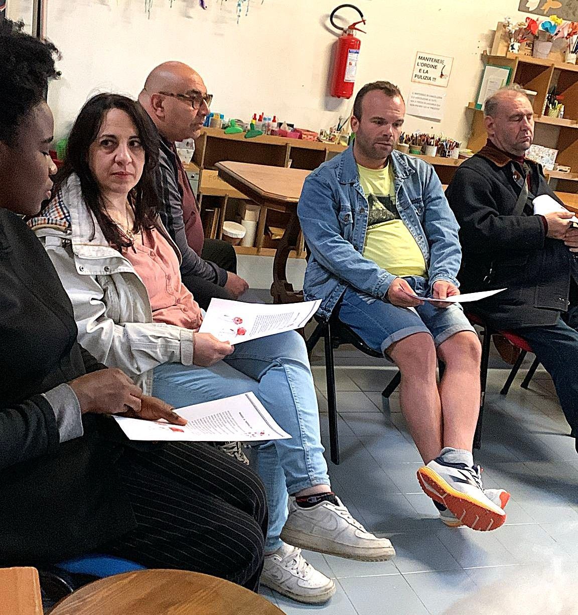 Un gruppo di persone sedute in una stanza, con in mano dei documenti e lo sguardo rivolto avanti.