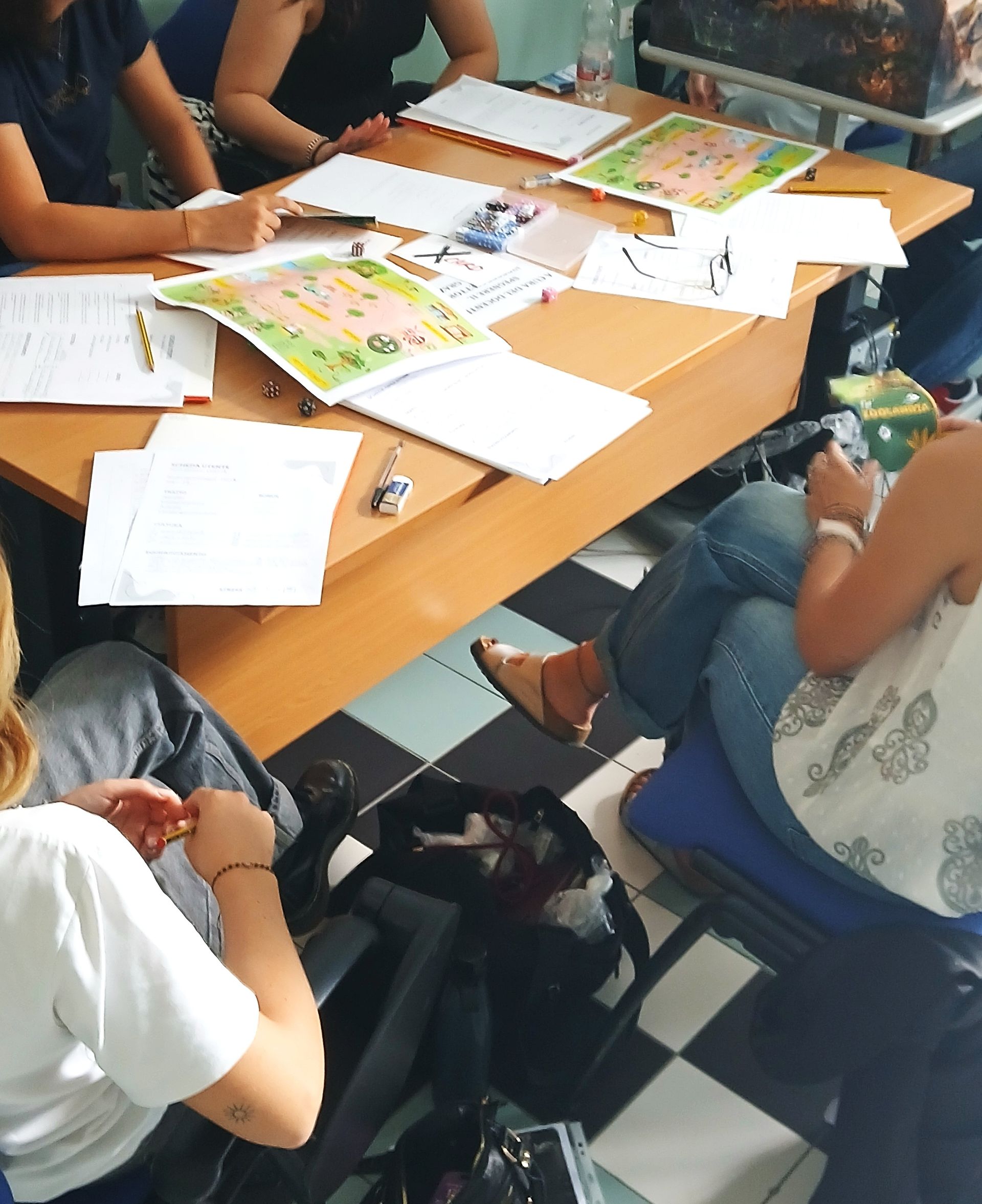Persone sedute attorno a un tavolo, che lavorano su documenti. Ambiente di classe, vista dall'alto.