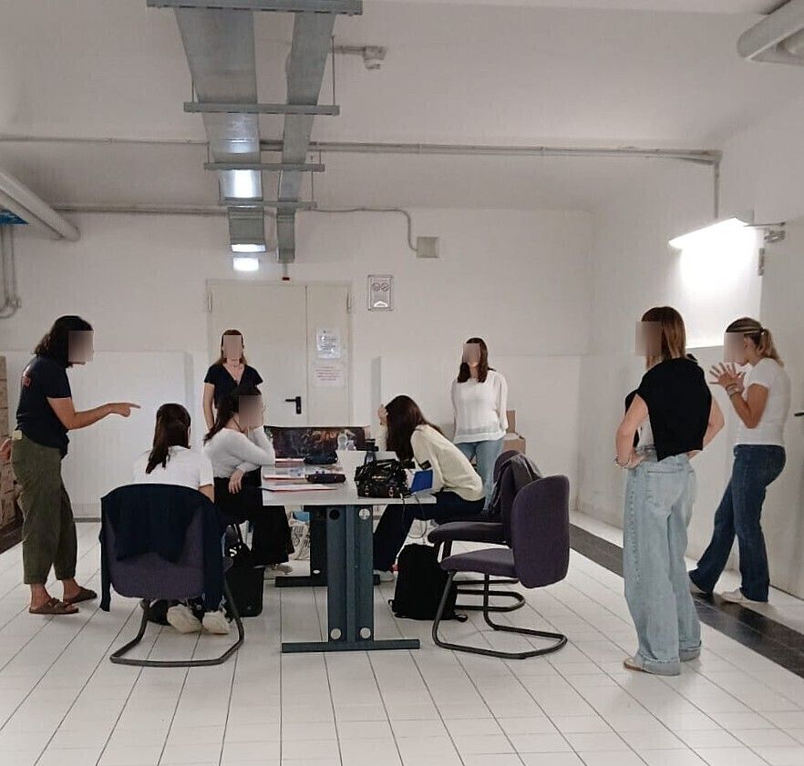 Un gruppo di persone in una stanza bianca, attorno a un tavolo, alcune in piedi e altre sedute, erano impegnate in una discussione.