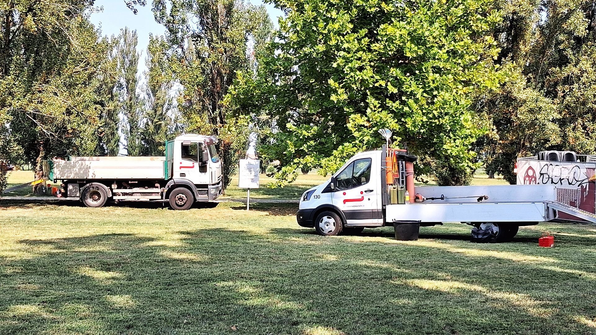 Due camion parcheggiati sull'erba in un parco, con alberi sullo sfondo.