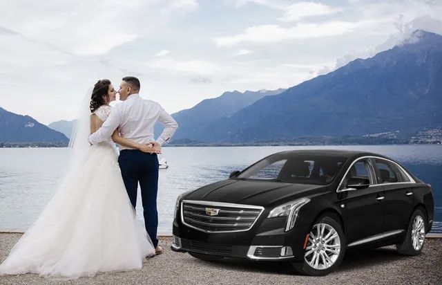 A bride and groom are kissing in front of a black car.