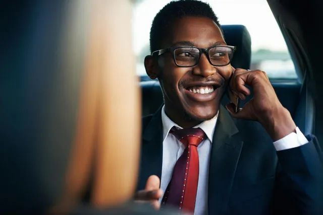 A man in a suit and tie is talking on a cell phone in a car.
