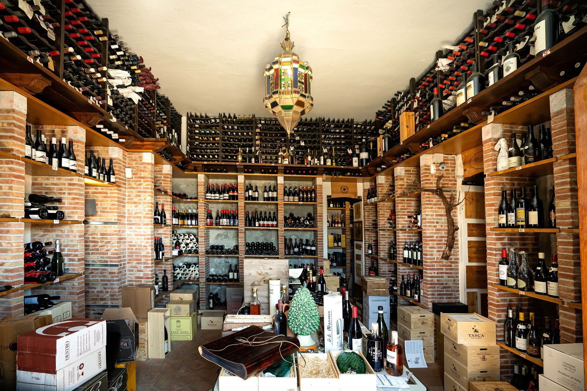 Interno di un'enoteca con scaffali pieni di bottiglie e un'esposizione centrale sotto una lanterna sospesa.