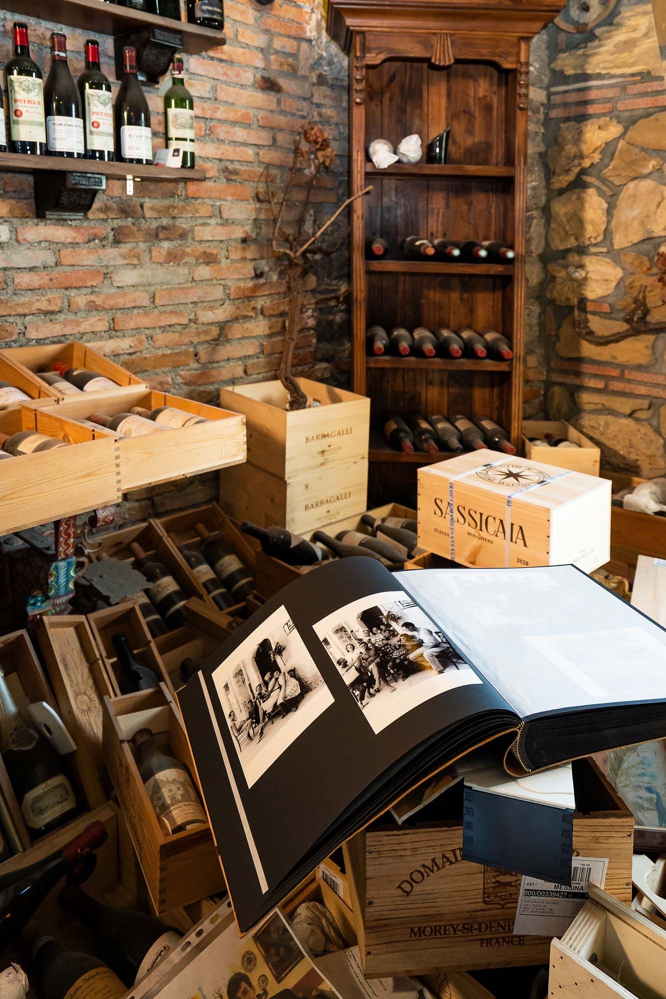Accogliente cantina con bottiglie, scaffali in legno e album fotografici aperti su un tavolo rustico.