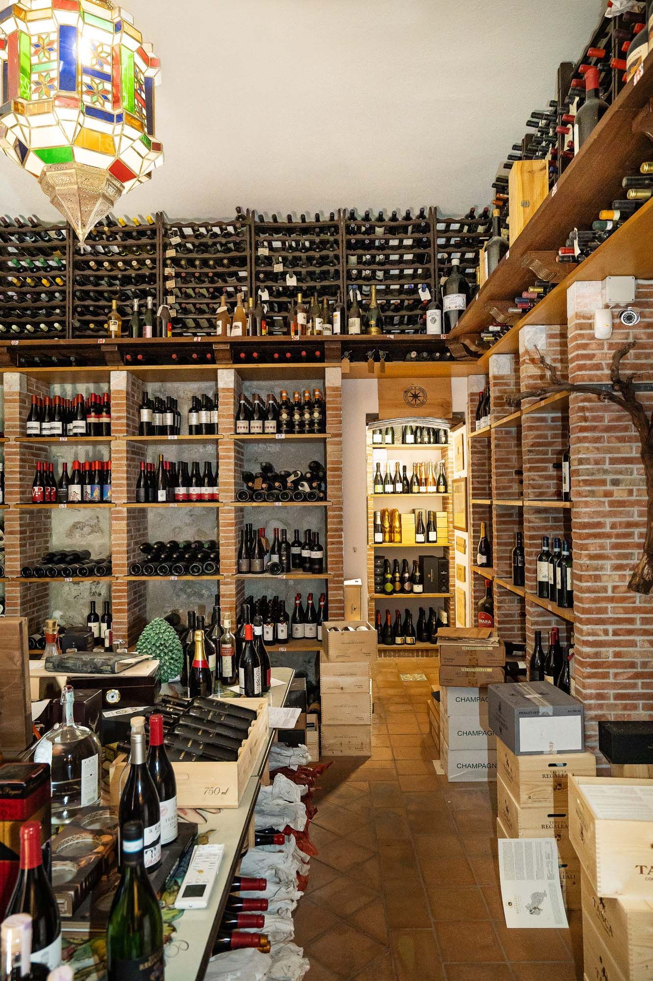 Interno di un'enoteca con scaffali di bottiglie, rastrelliere in legno e scatole impilate.
