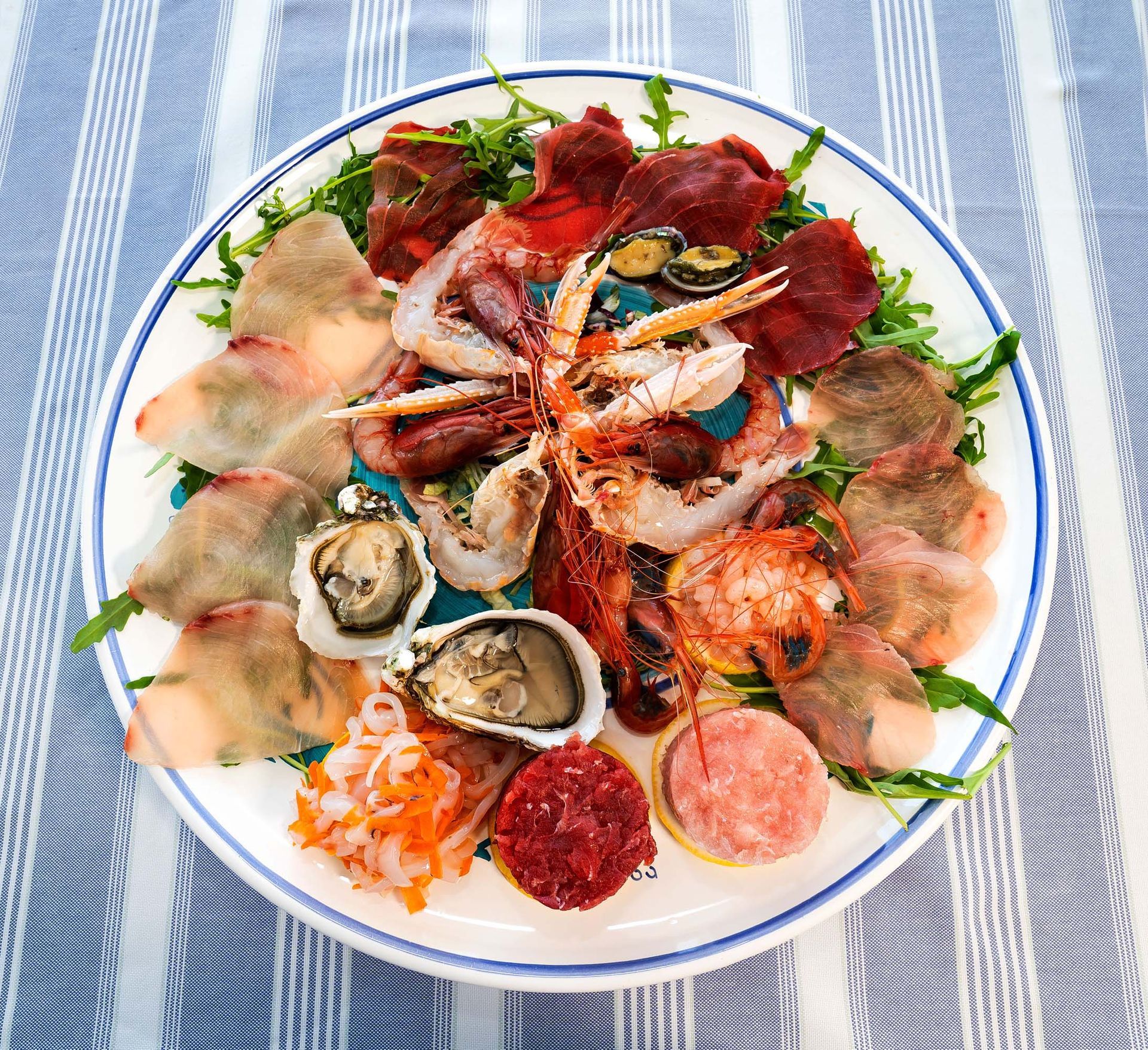 Assortimento di sushi e sashimi su un piatto bianco, con gamberi, ostriche e sottili fette di pesce.