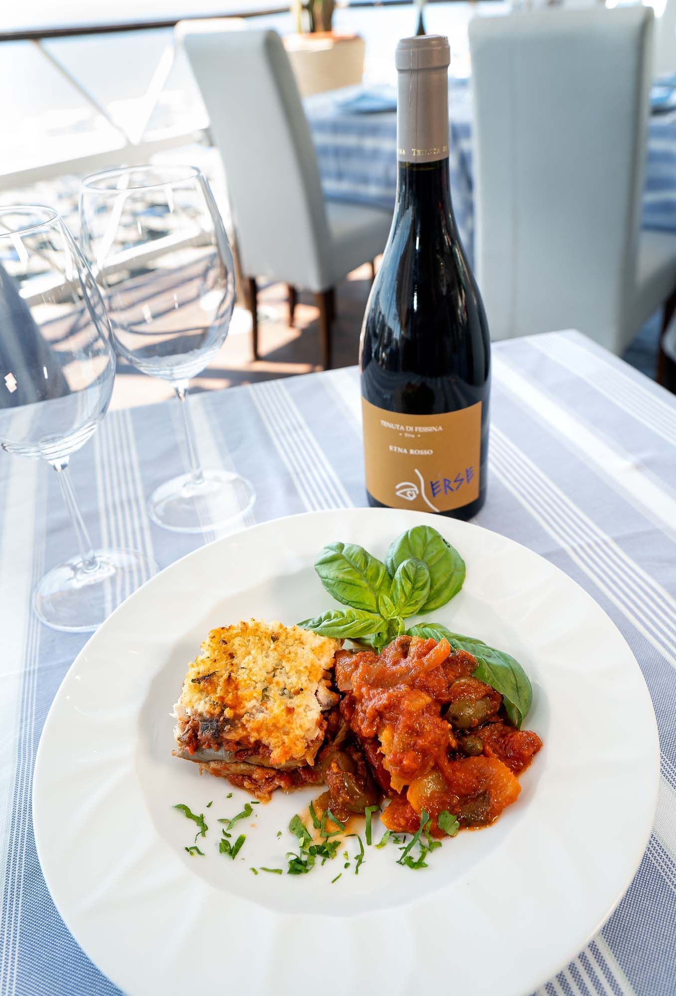 Piatto unico con salsa rossa accanto a una bottiglia di vino su un tavolo luminoso di un ristorante.