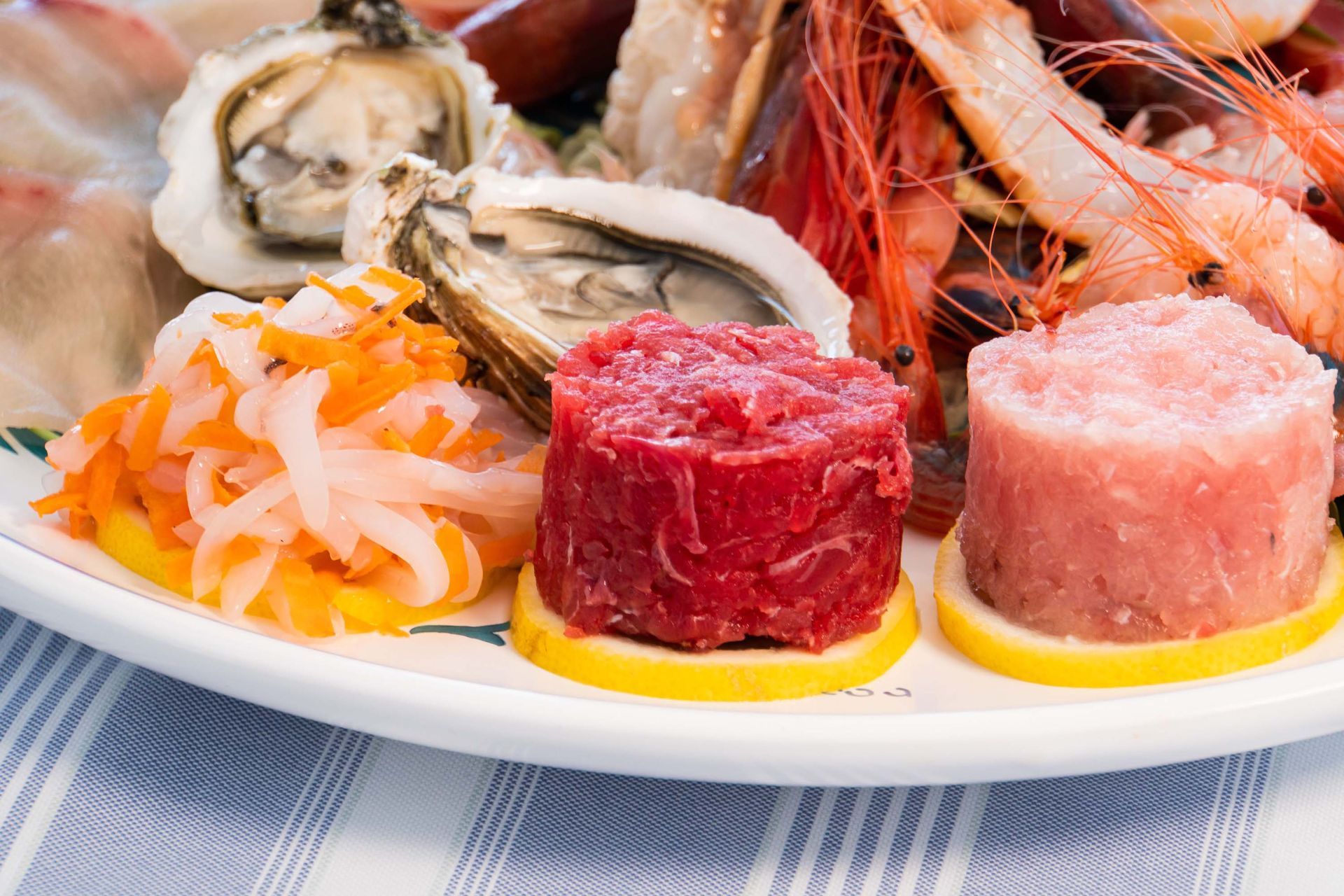 Piatto di frutti di mare con ostriche, gamberi, tartare di salmone e tonno a cubetti su un piatto bianco.