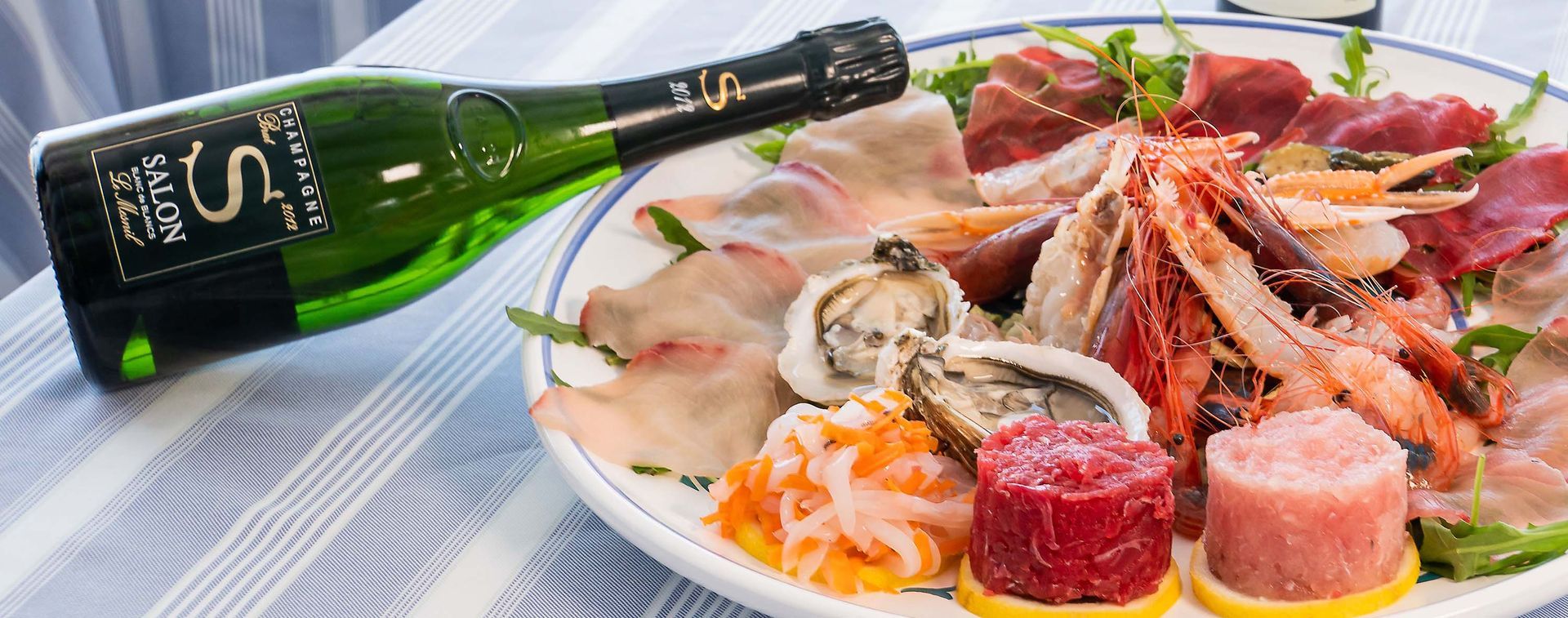 Una bottiglia di champagne accanto a un piatto di frutti di mare con ostriche, gamberi, granchio e affettati su un tavolo.