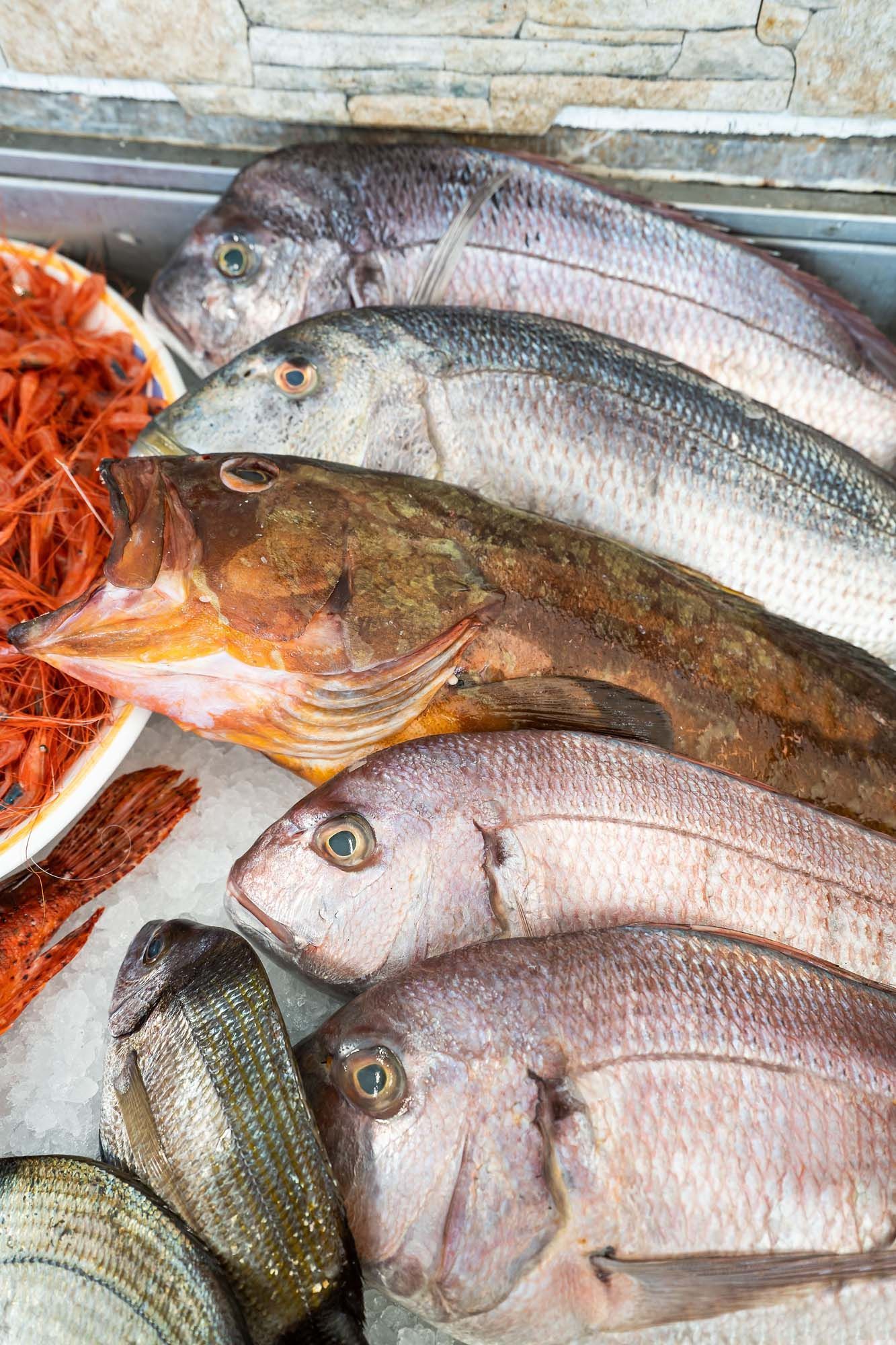 Pesce intero fresco e frutti di mare arancioni su ghiaccio in una bancarella del mercato