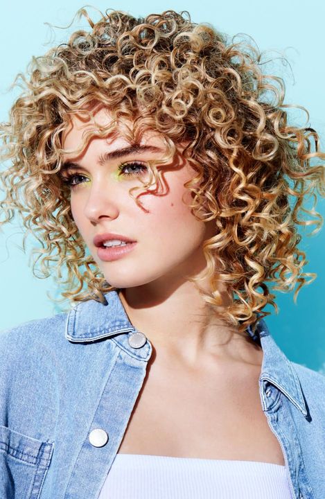 I capelli biondi coprono parzialmente il viso, scendendo verso il basso. Donna che indossa un top decorato, guarda a sinistra.