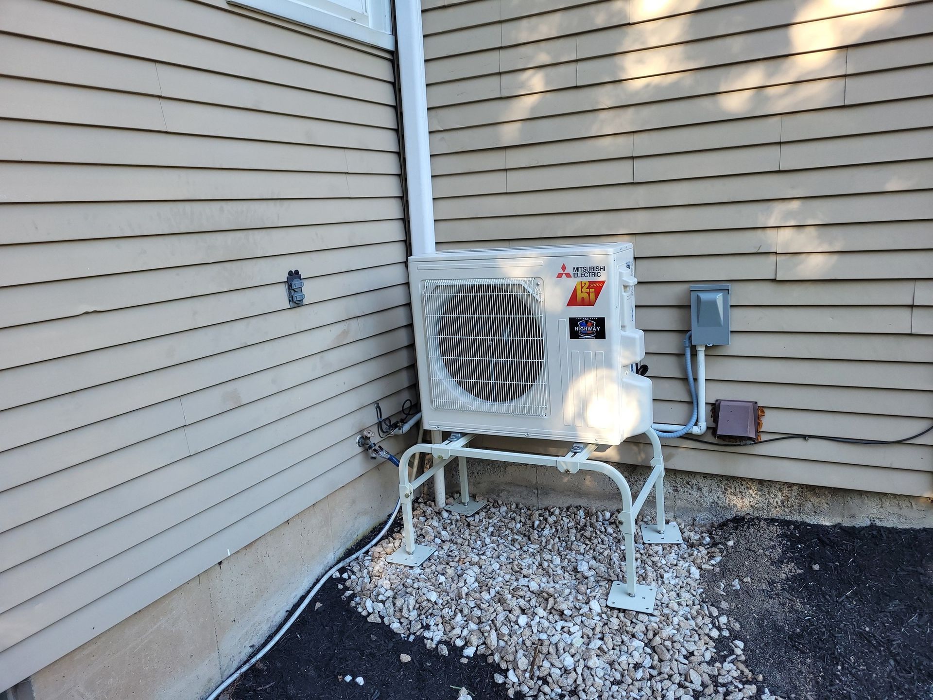 Outdoor air conditioner unit on white gravel beside beige house siding.