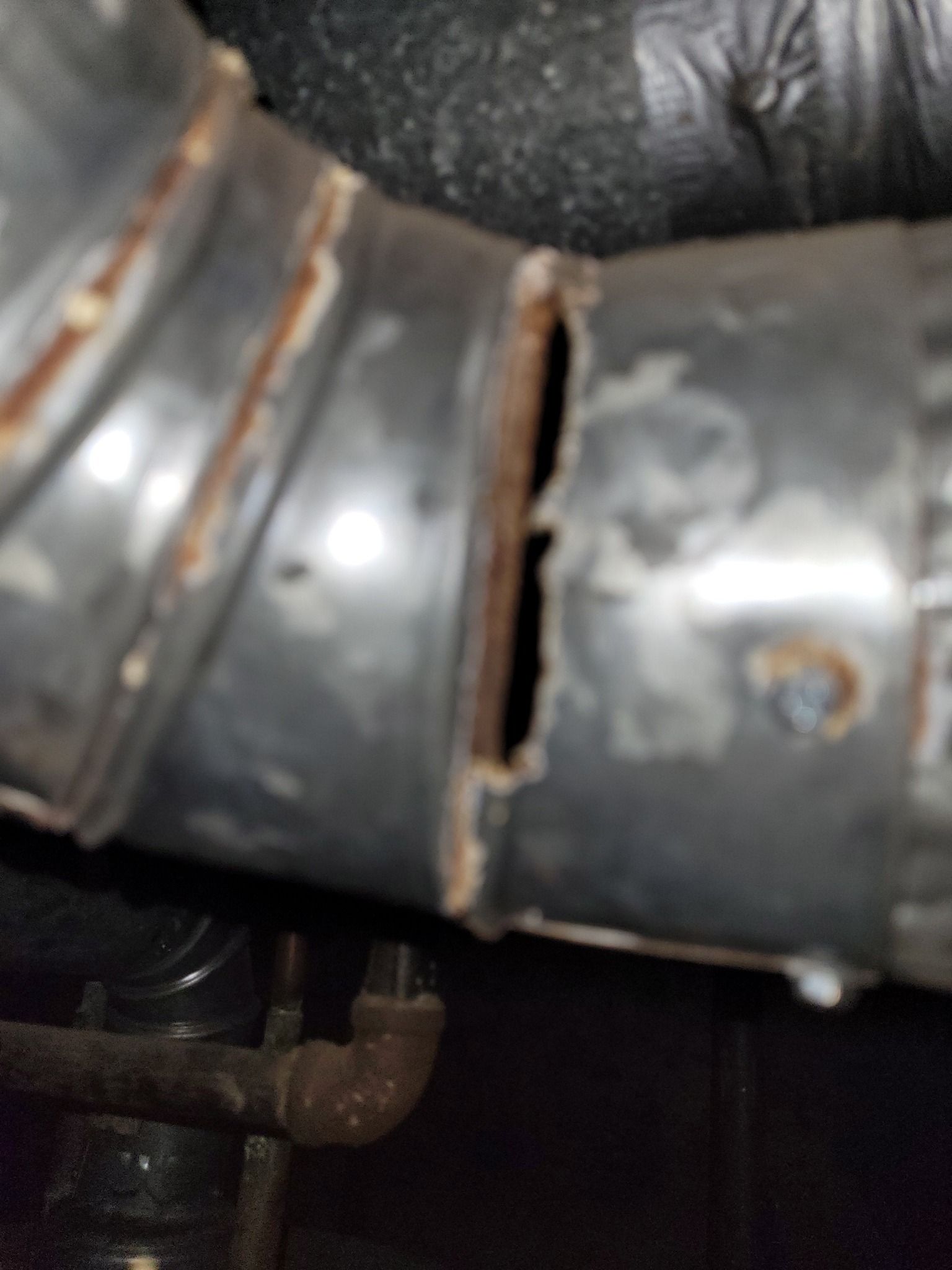 Close-up of a damaged metal pipe joint with a rusted crack and black bands