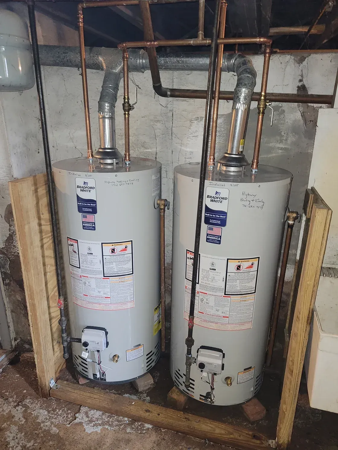 Two water heaters in a basement utility area with exposed pipes and wooden framing