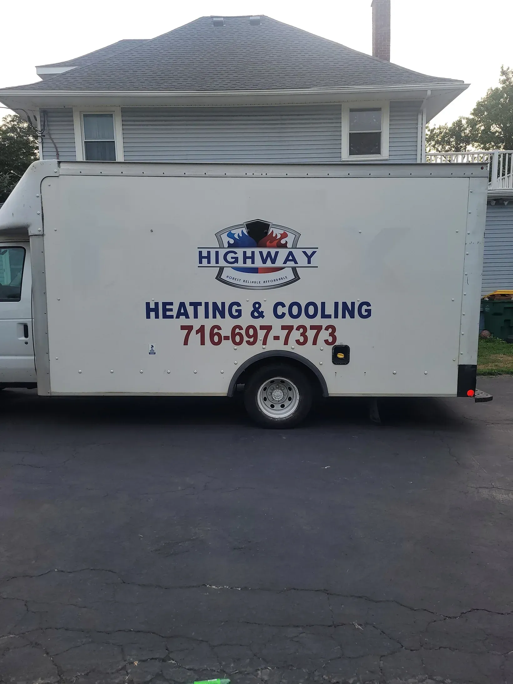 White HVAC service truck with logo and phone number parked on a driveway in front of a house