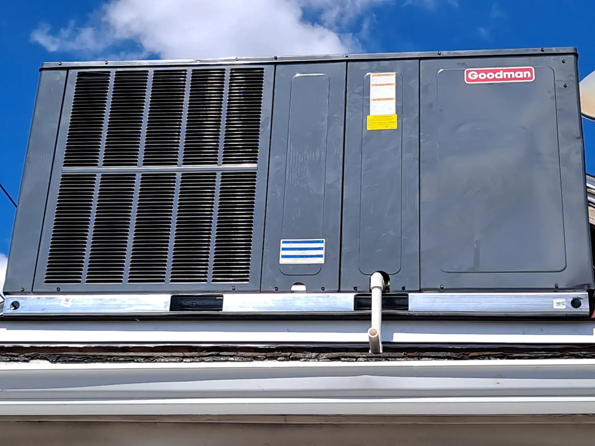 Large gray rooftop HVAC unit with vents and a red label against a blue sky