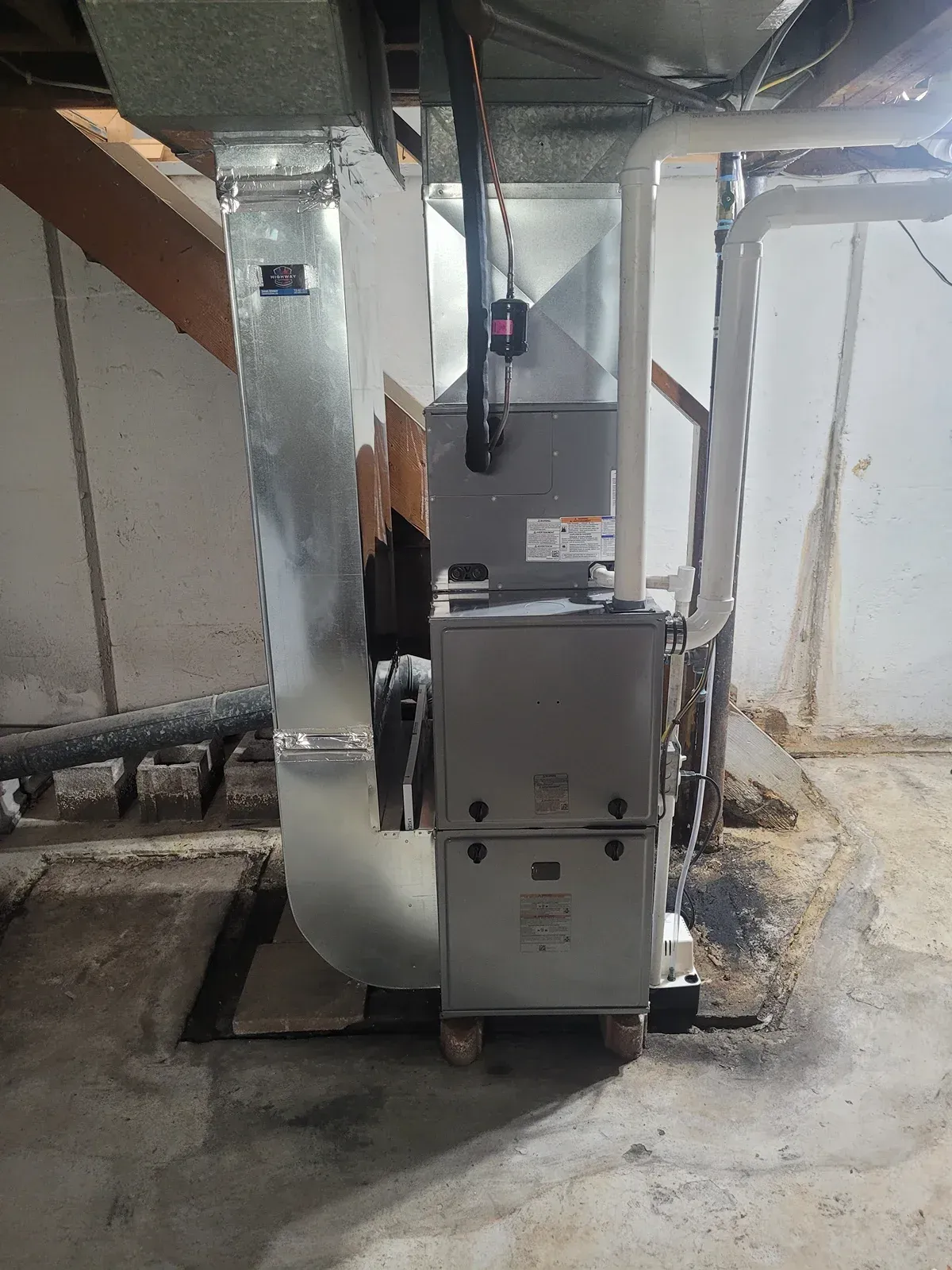 Basement HVAC ductwork and furnace unit with silver metal vents and white piping