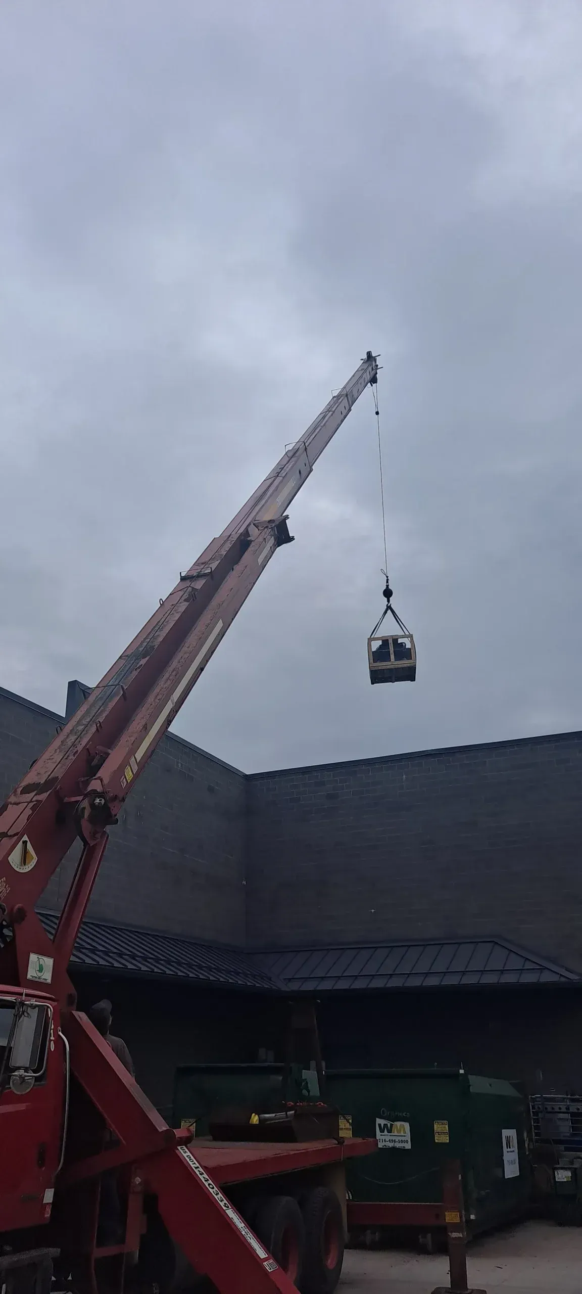 Crane lifting a small cable car pod over a large stadium under a cloudy sky