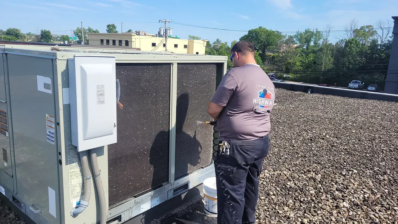 Technician inspecting a rooftop HVAC unit with a damaged fan grille under a clear sky