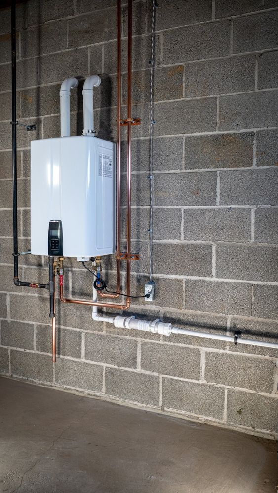 Wall-mounted white water heater with copper and PVC pipes in a cinder block utility room