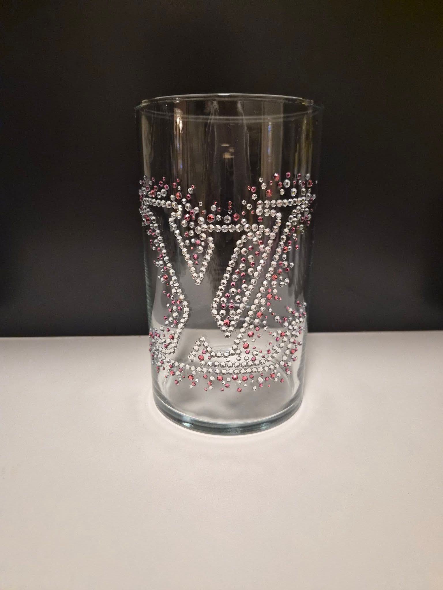Doorzichtig glazen drinkglas met een roze V-vormig stippenpatroon op een grijze ondergrond.