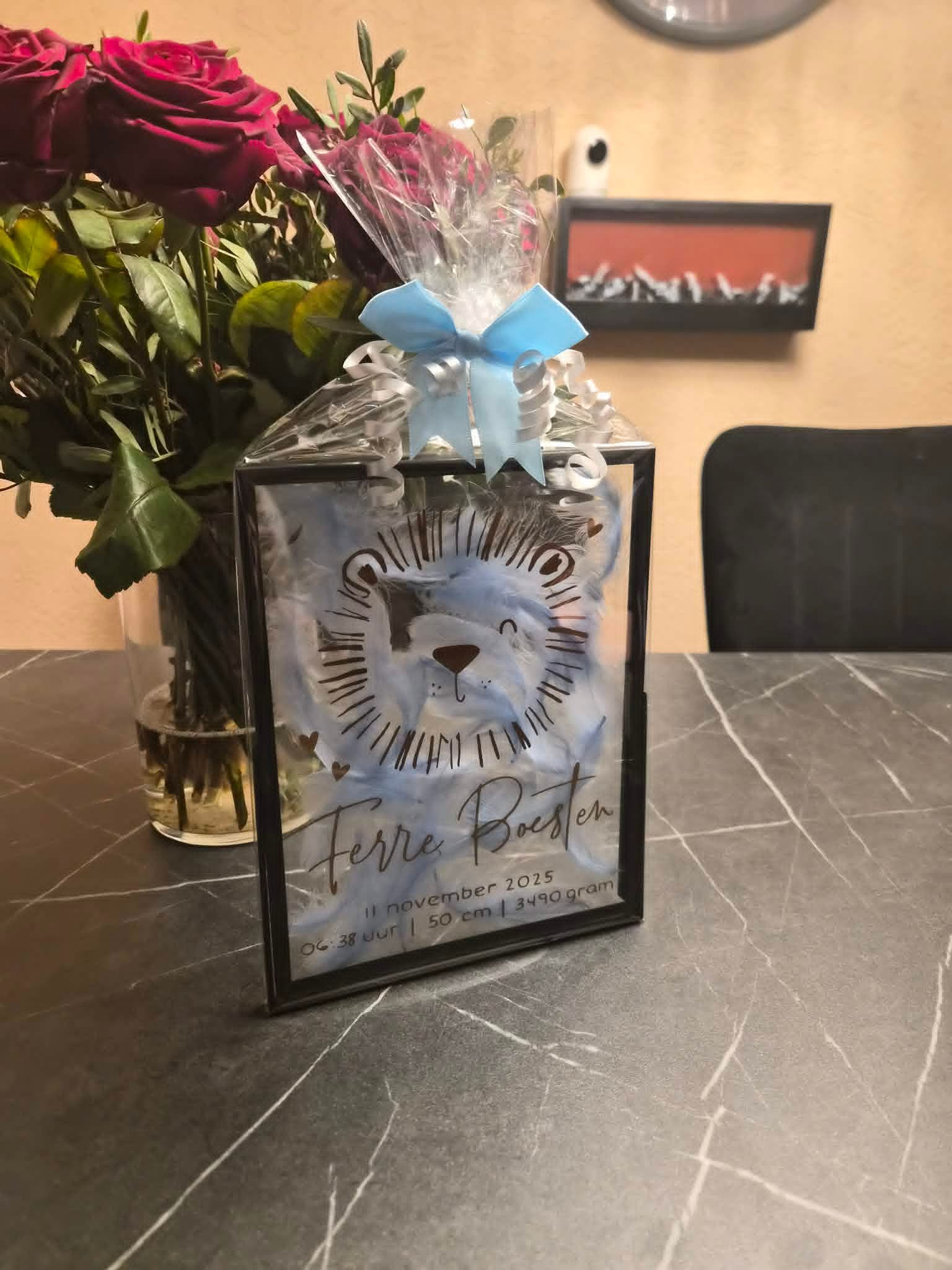 Decoratieve geschenkdoos met blauwe strik en transparante folie op een eettafel naast een boeket rode rozen.