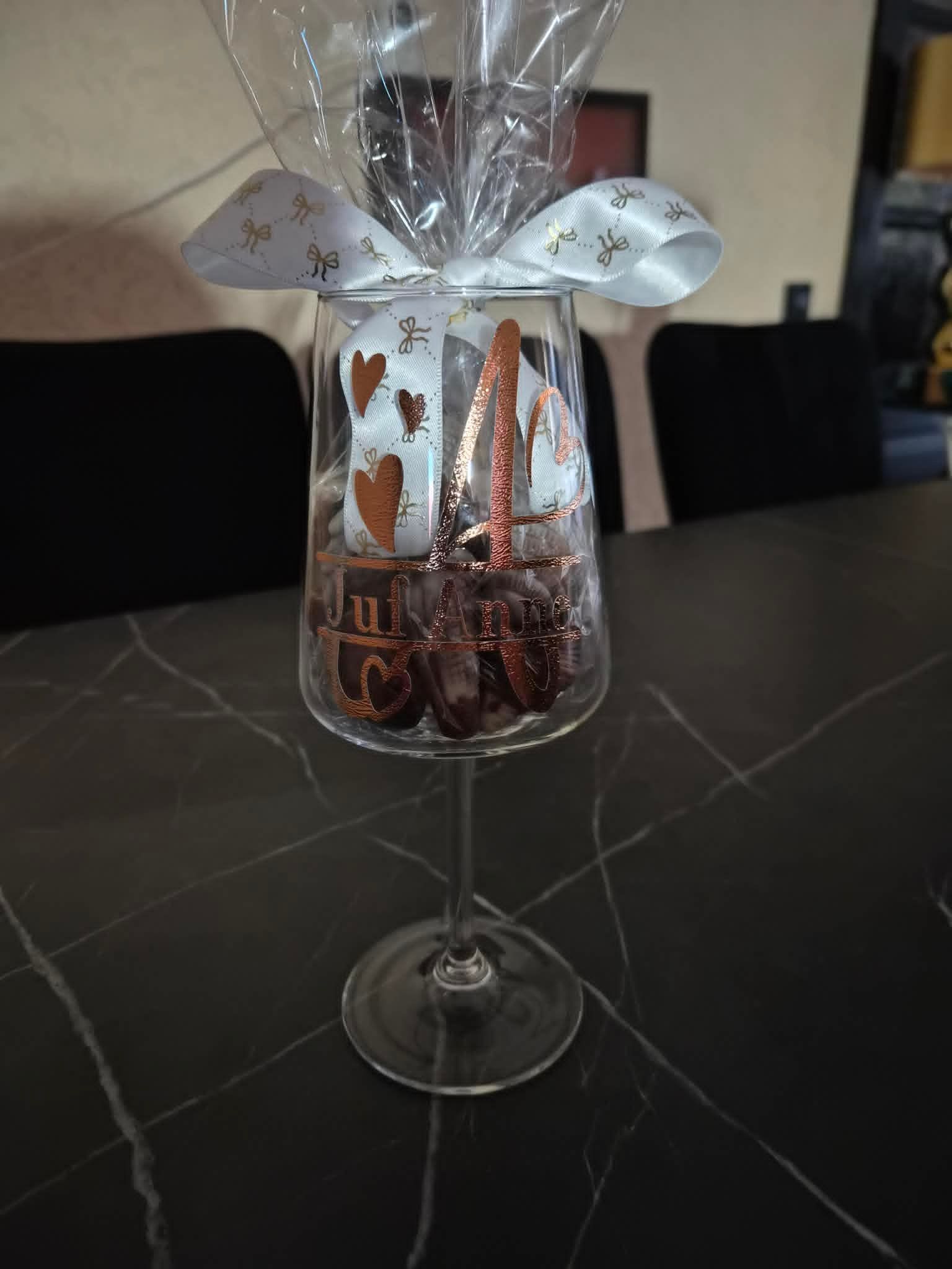 Een doorzichtige geschenkzak met chocolaatjes en een lint op een wijnglazenhouder op een zwarte marmeren tafel.