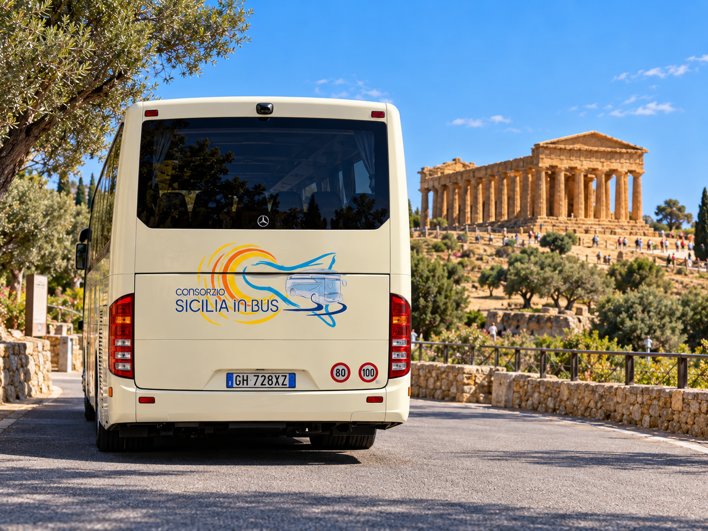Autobus bianco su una strada, di fronte a un alto monumento moderno bianco, sotto un cielo azzurro e terso.
