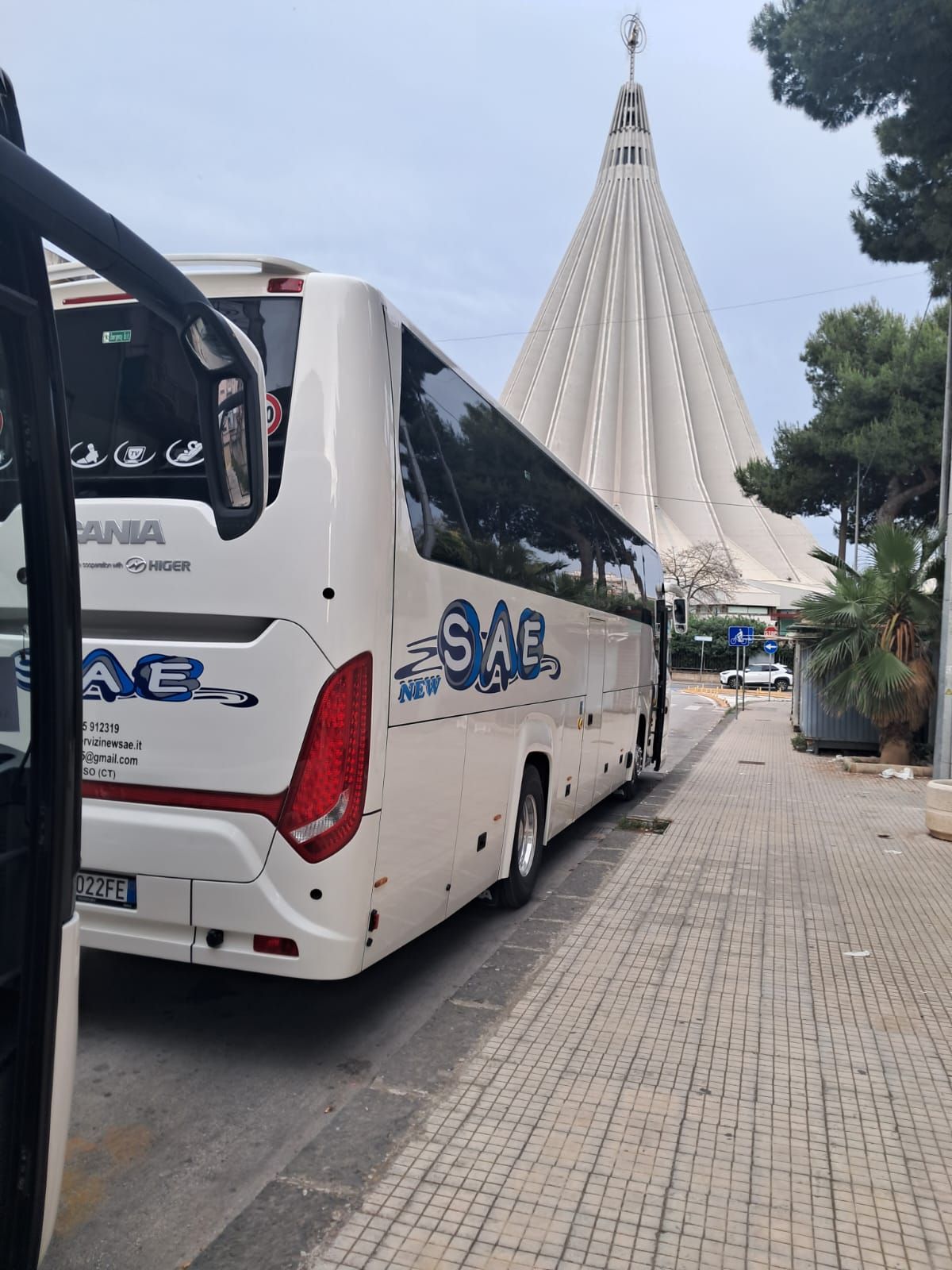 Autobus in una piazza allagata vicino a un alto monumento, sotto un cielo azzurro nuvoloso