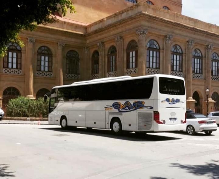 Pullman bianco parcheggiato davanti a un grande edificio in mattoni con finestre ad arco e un’auto bianca nelle vicinanze