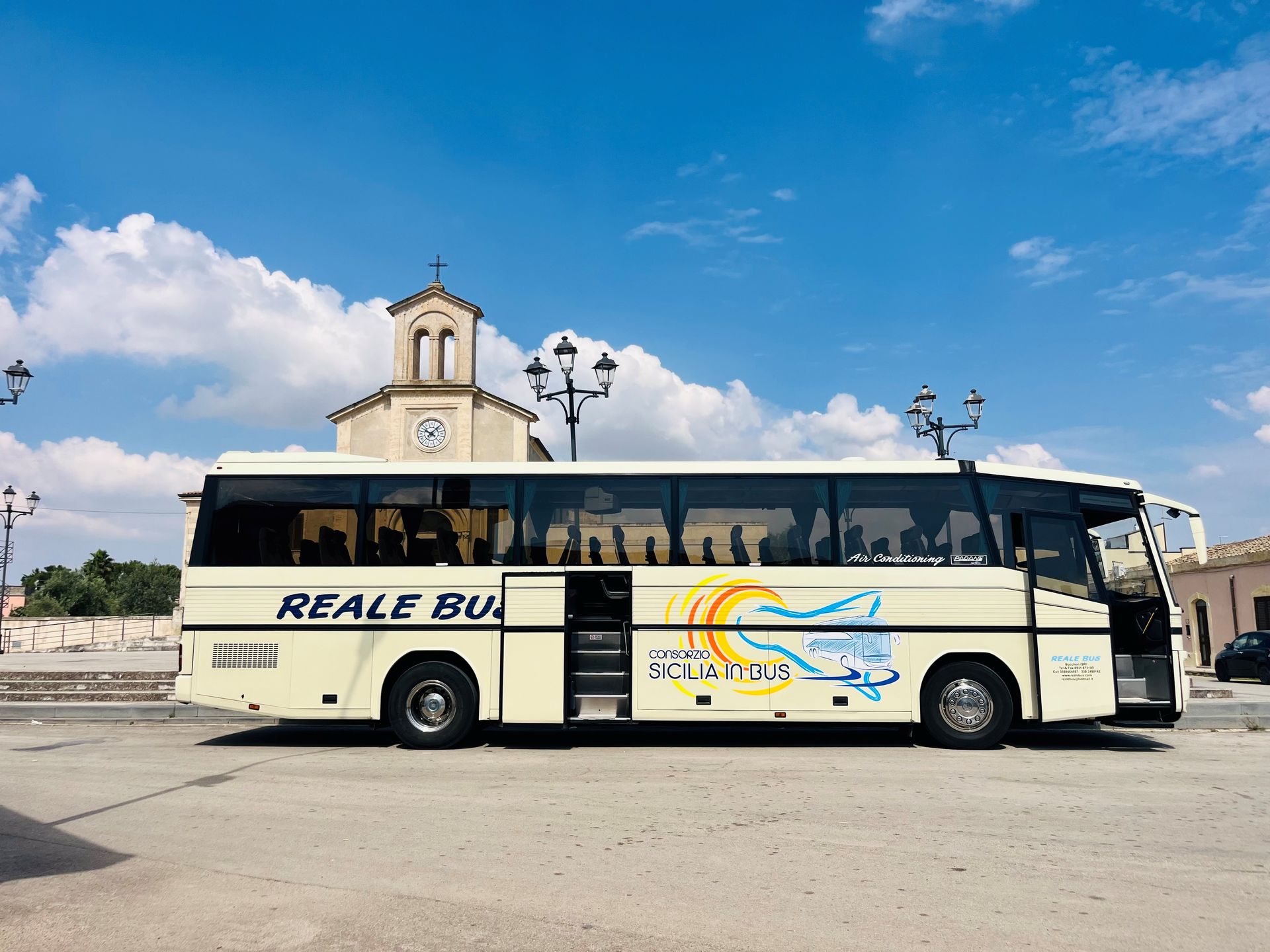 Autobus color crema parcheggiato vicino a una chiesa sotto un cielo azzurro con nuvole